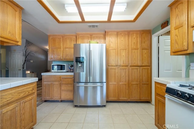 kitchen with vaulted ceiling, tile countertops, light tile patterned flooring, and white appliances