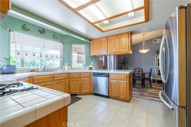 kitchen featuring kitchen peninsula, appliances with stainless steel finishes, sink, decorative light fixtures, and tile countertops