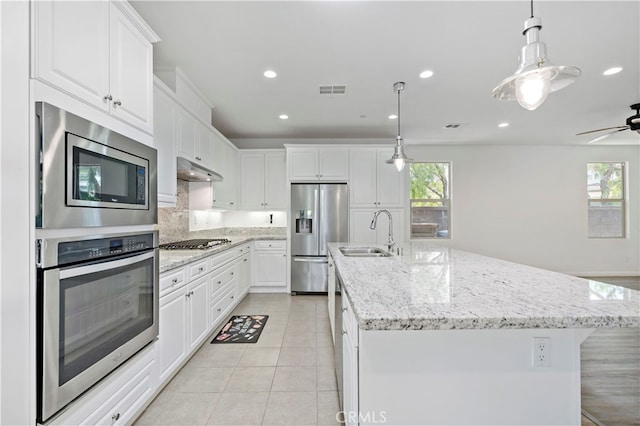 kitchen with stainless steel appliances, decorative light fixtures, an island with sink, and white cabinets