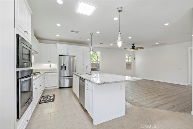 kitchen featuring stainless steel appliances, a center island with sink, decorative light fixtures, white cabinetry, and light hardwood / wood-style floors