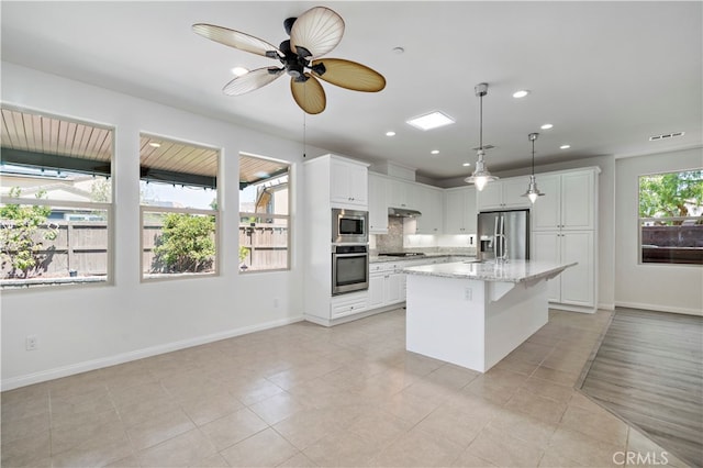 kitchen with white cabinets, a kitchen island with sink, light stone countertops, pendant lighting, and stainless steel appliances