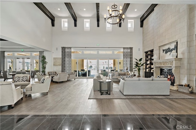 living room with a high ceiling, beam ceiling, wood-type flooring, a large fireplace, and a notable chandelier