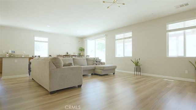 living room with plenty of natural light, light hardwood / wood-style floors, and an inviting chandelier