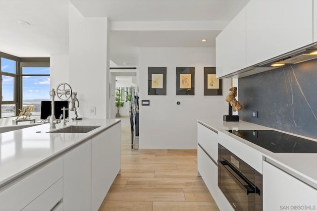 kitchen featuring sink, white cabinets, light hardwood / wood-style floors, black appliances, and decorative backsplash