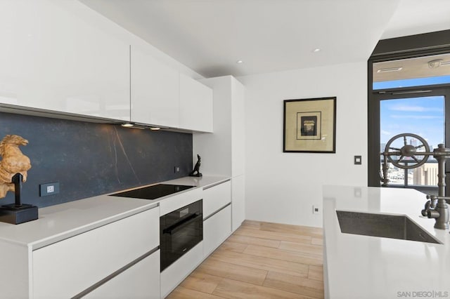 kitchen with white cabinets, black appliances, tasteful backsplash, sink, and light hardwood / wood-style flooring