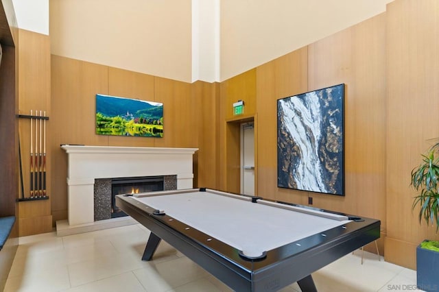 game room featuring a towering ceiling, wooden walls, and light tile patterned floors