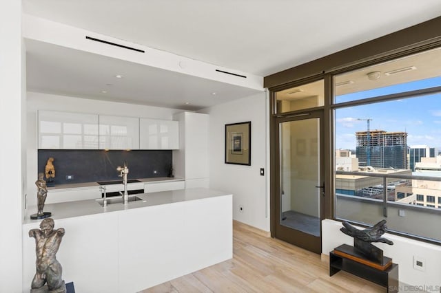 kitchen with sink, light hardwood / wood-style floors, white cabinetry, and decorative backsplash