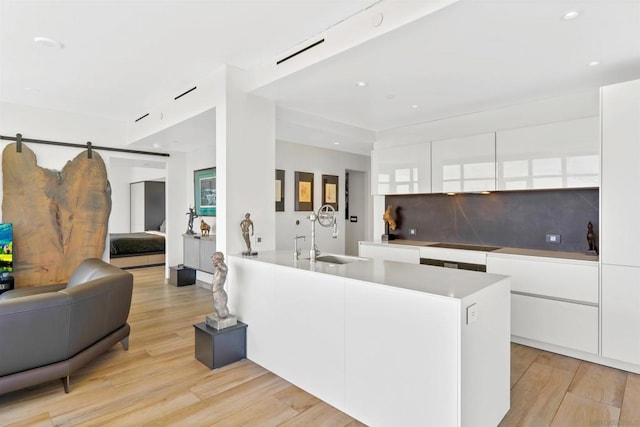 kitchen with sink, light wood-type flooring, white cabinetry, a barn door, and black electric cooktop