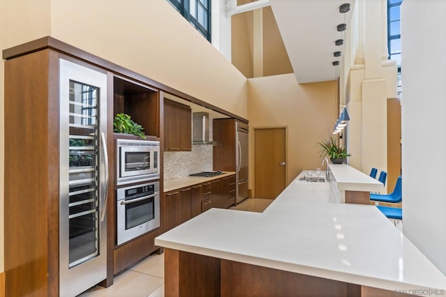 kitchen featuring appliances with stainless steel finishes, wall chimney exhaust hood, light tile patterned floors, a high ceiling, and decorative backsplash