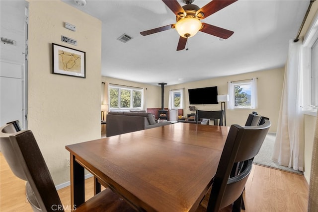 dining space featuring a wood stove, light hardwood / wood-style floors, and ceiling fan