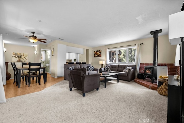 living room featuring ceiling fan, light carpet, and a wood stove