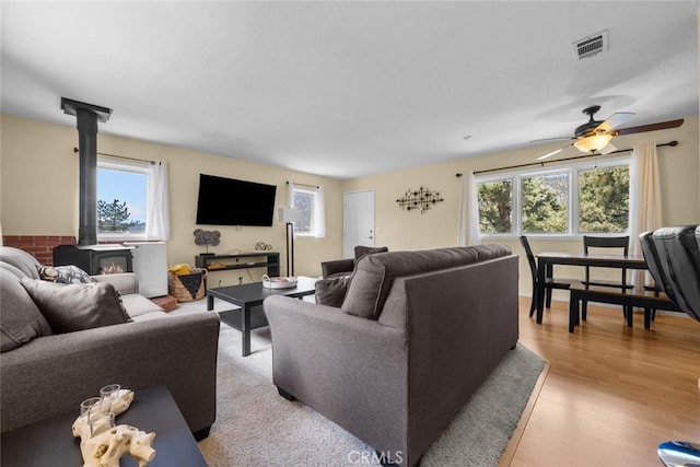 living room featuring light hardwood / wood-style floors, ceiling fan, a wood stove, and a wealth of natural light