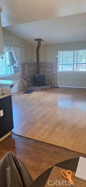 unfurnished living room featuring vaulted ceiling, a wood stove, and hardwood / wood-style floors