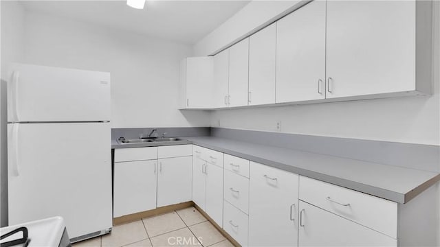 kitchen with sink, light tile patterned floors, range, white cabinetry, and white fridge