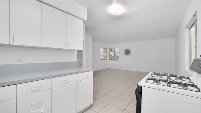 kitchen with white gas range, white cabinets, and light tile patterned flooring