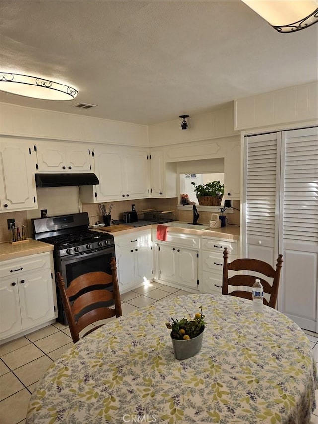 kitchen with light tile patterned floors, under cabinet range hood, stainless steel range with gas stovetop, and white cabinets