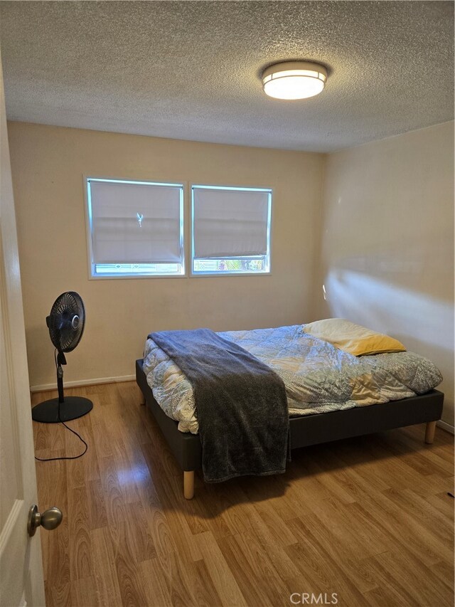 bedroom with wood finished floors, baseboards, and a textured ceiling