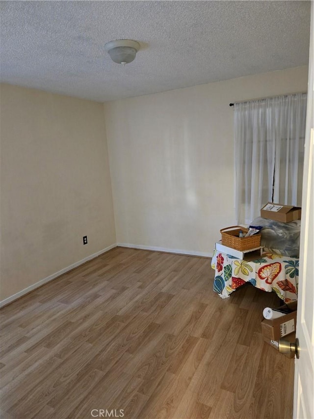 spare room featuring baseboards, a textured ceiling, and wood finished floors