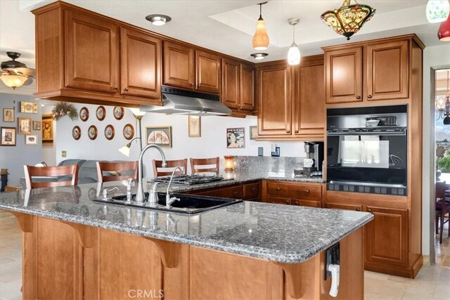 kitchen with a kitchen breakfast bar, dark stone counters, sink, black oven, and hanging light fixtures