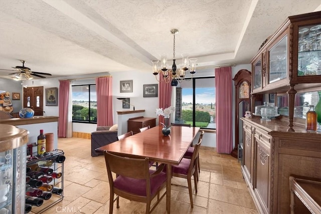 dining room featuring ceiling fan with notable chandelier, a raised ceiling, and a textured ceiling