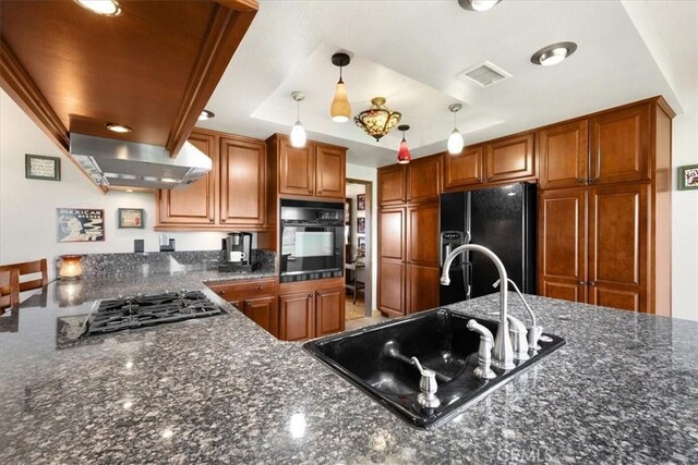 kitchen with ventilation hood, a tray ceiling, sink, black appliances, and hanging light fixtures