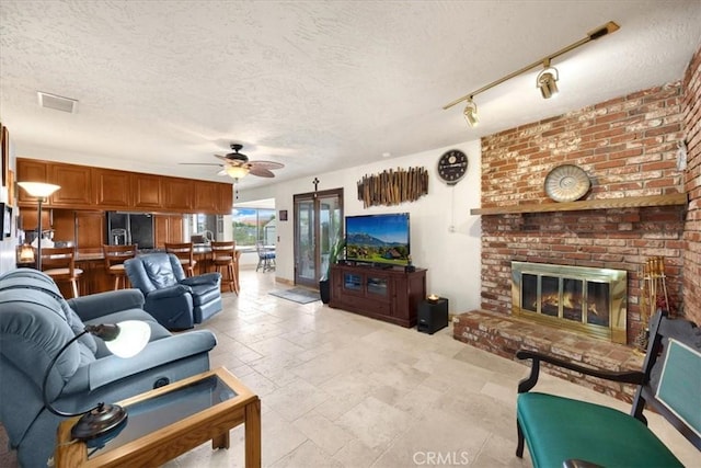 living room with ceiling fan, a fireplace, and a textured ceiling