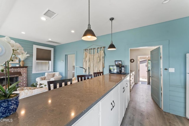 kitchen with white cabinetry, a brick fireplace, wood-type flooring, dark stone counters, and decorative light fixtures