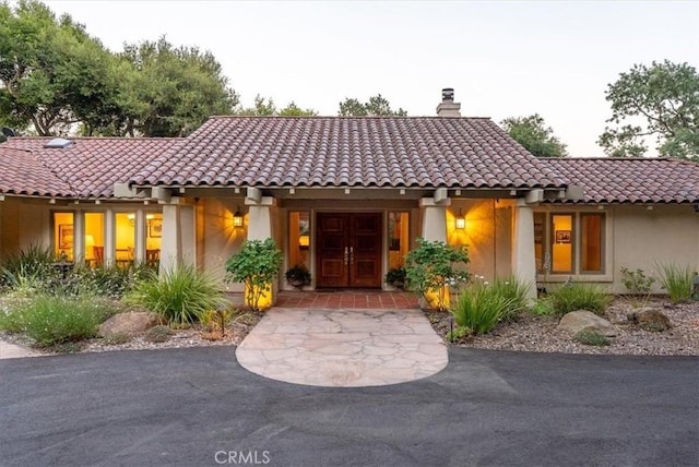 mediterranean / spanish-style house featuring a chimney, a tile roof, and stucco siding