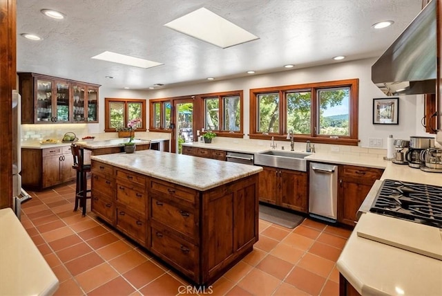 kitchen featuring a skylight, a center island, light countertops, a sink, and extractor fan