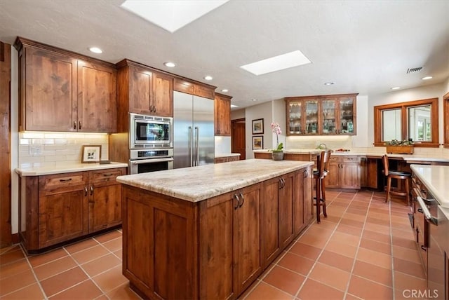 kitchen featuring a skylight, tasteful backsplash, a kitchen island, tile patterned floors, and built in appliances