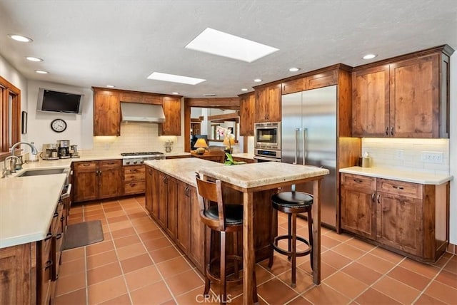 kitchen with built in appliances, light tile patterned floors, a skylight, a sink, and exhaust hood