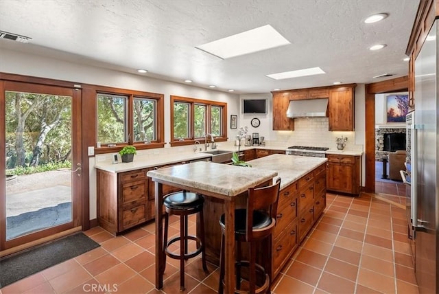 kitchen featuring a skylight, visible vents, brown cabinetry, light countertops, and under cabinet range hood