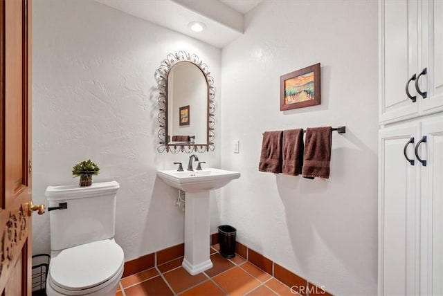 half bathroom featuring a textured wall, tile patterned flooring, toilet, a sink, and baseboards