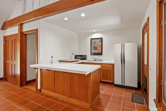 kitchen featuring black microwave, a peninsula, dark tile patterned flooring, freestanding refrigerator, and brown cabinetry