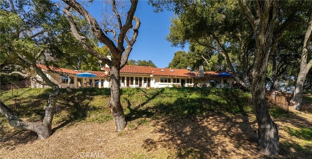 rear view of house featuring a fenced front yard and a tiled roof