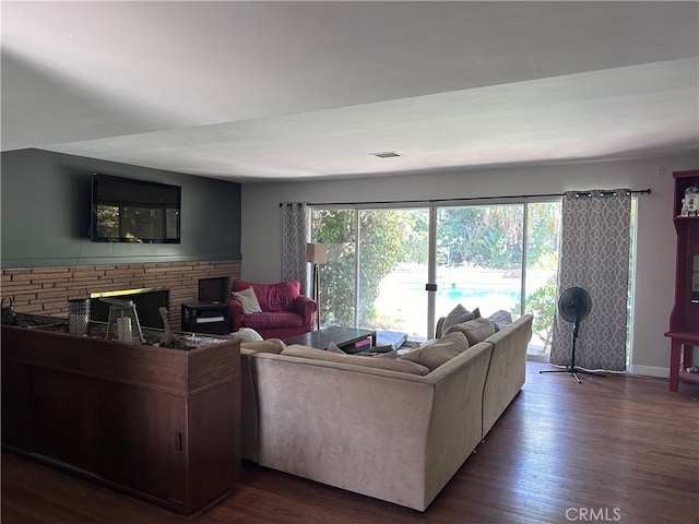 living room featuring a brick fireplace and dark wood-type flooring