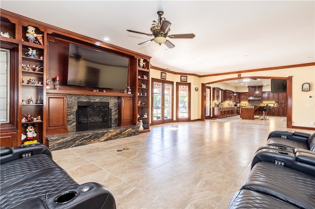 living area with ceiling fan, built in shelves, a premium fireplace, french doors, and ornamental molding