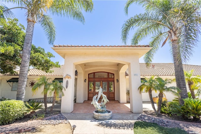 view of exterior entry featuring french doors, a tiled roof, and stucco siding