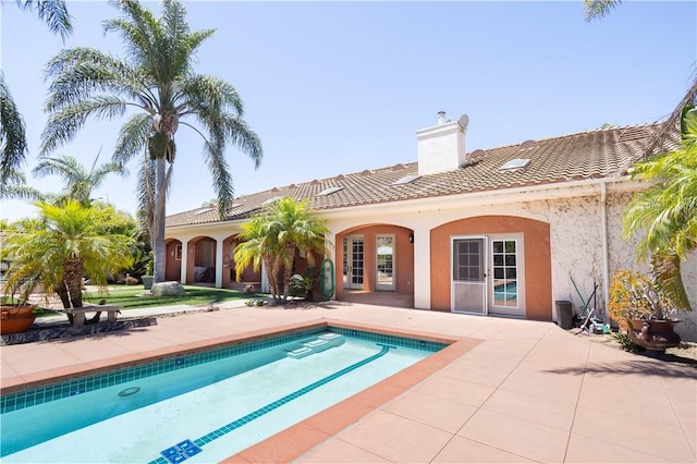 rear view of house with a chimney, an outdoor pool, a tile roof, and stucco siding