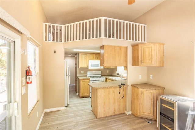 kitchen featuring white appliances, light countertops, light brown cabinetry, light wood-style floors, and a sink