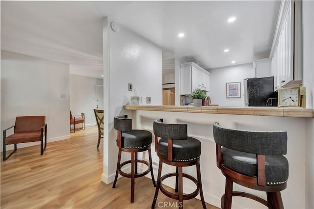 kitchen featuring a kitchen bar, black refrigerator, light wood-type flooring, tile countertops, and white cabinets