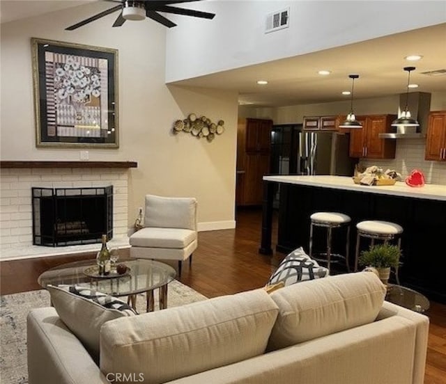 living room featuring ceiling fan, dark hardwood / wood-style flooring, vaulted ceiling, and a brick fireplace