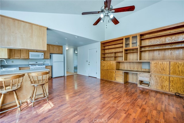 kitchen with white appliances, kitchen peninsula, a breakfast bar area, ceiling fan, and hardwood / wood-style floors