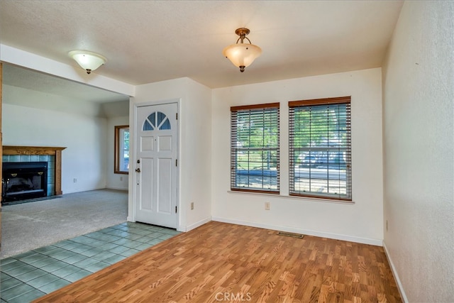 unfurnished living room featuring a textured ceiling, light hardwood / wood-style floors, and a tiled fireplace