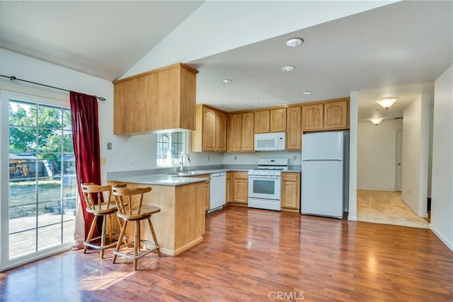 kitchen featuring a breakfast bar, light hardwood / wood-style floors, vaulted ceiling, kitchen peninsula, and white appliances