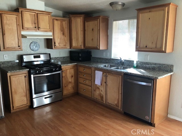 kitchen with sink, stainless steel appliances, dark stone countertops, and wood-type flooring