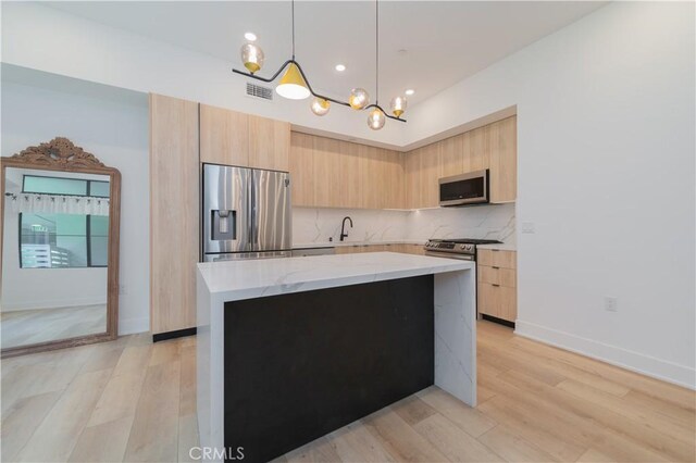 kitchen with light stone countertops, hanging light fixtures, stainless steel appliances, light hardwood / wood-style flooring, and light brown cabinets