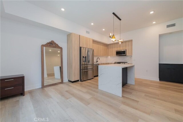 kitchen featuring light stone countertops, appliances with stainless steel finishes, light wood-type flooring, decorative light fixtures, and decorative backsplash