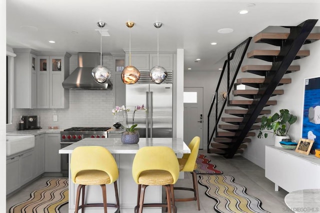 kitchen featuring wall chimney exhaust hood, high quality appliances, decorative light fixtures, gray cabinets, and tasteful backsplash