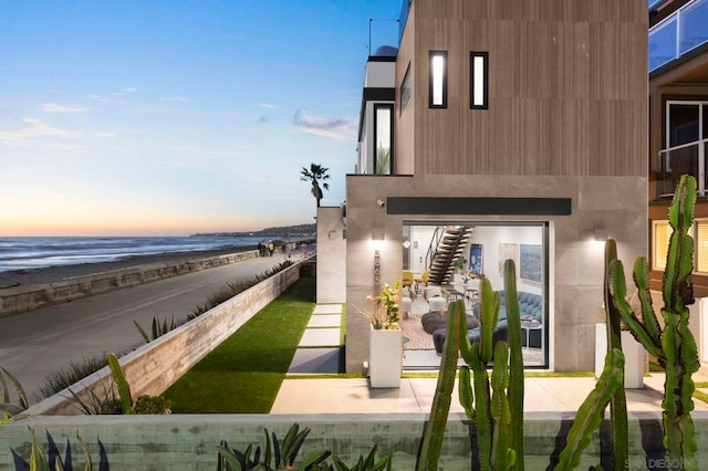 back house at dusk with a water view and a beach view